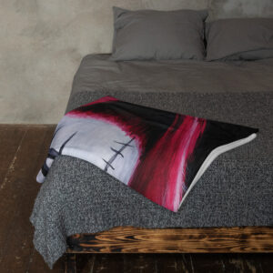 Top-down view of a bed with gray sheets and a bold red-and-black pillow on a dark rug and wooden bed frame visible at the foot of the bed.