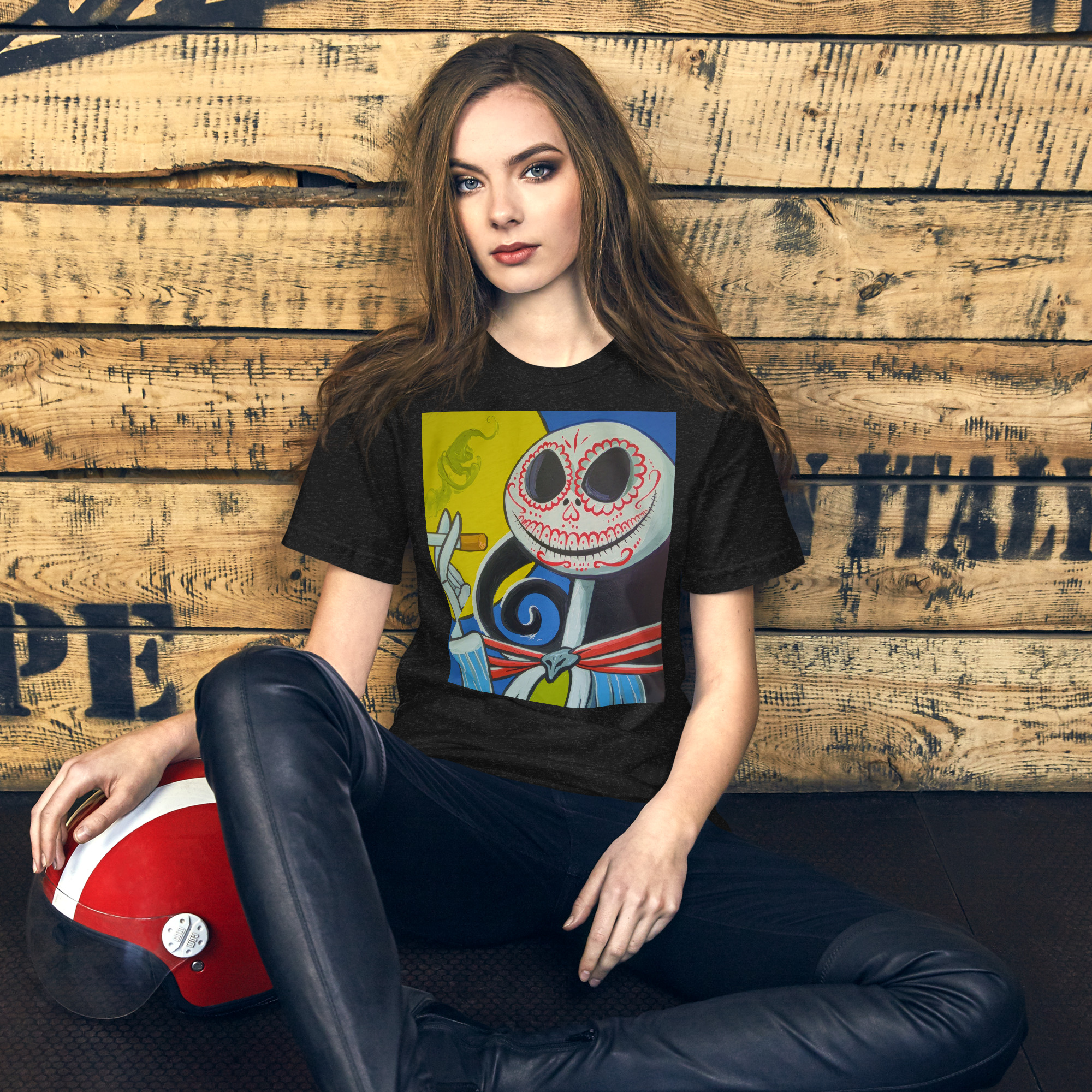 Young woman seated against a weathered wooden wall, wearing a black graphic T-shirt and holding a red-and-white helmet near her leg.